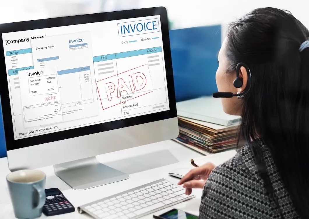 A support agent wearing a headset looking at an invoice marked paid on screen