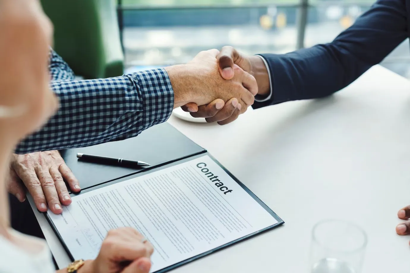 Two people shaking hands over a contract on a clipboard